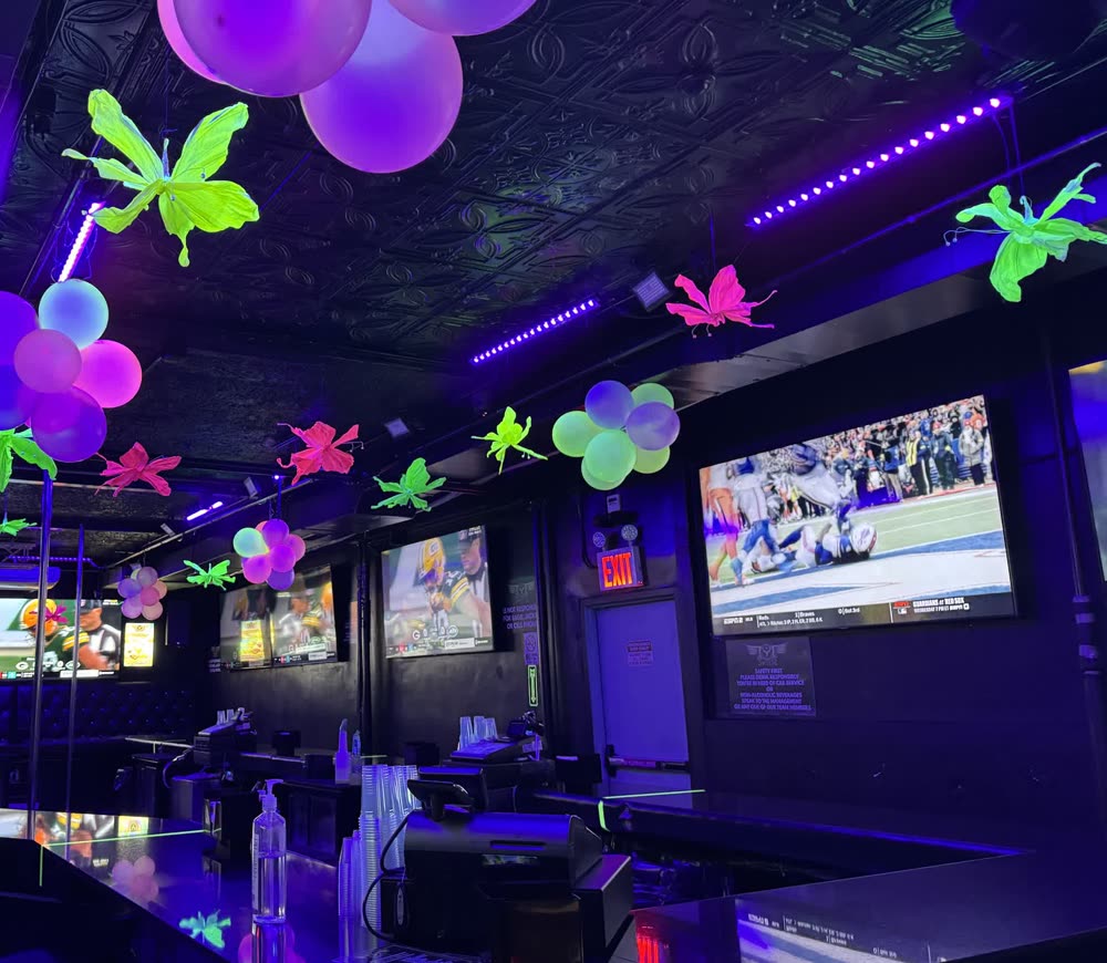 The bar at Sweets of NY with purple and pink balloons and neon green and pink butterflies overhead, and football on the big screens along the wall.
