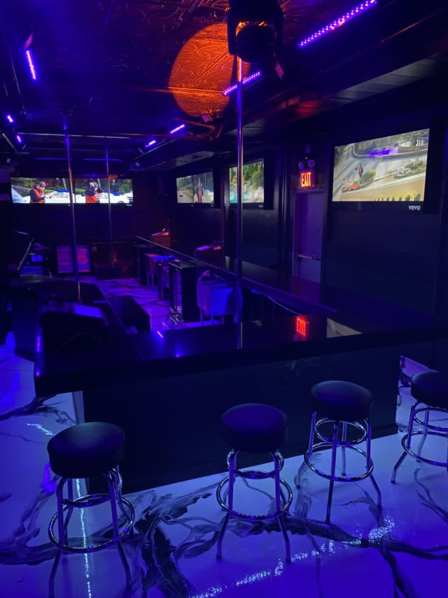 The long bar at Sweets of NY under blue light, stools along the counter, screens on the far wall and the marble floor in front.